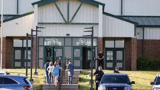 Law enforcement stand outside of Henryetta High School as people arrive for a vigil after Okmulgee County Sheriff reported seven people dead after a search for two missing teenage girls