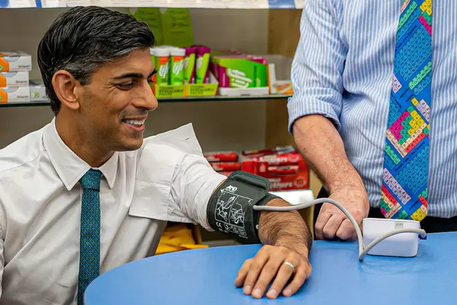 Britain's Prime Minister Rishi Sunak reacts as he has his blood pressure checked by pharmacist Peter Baillie, during a visit to a GP surgery