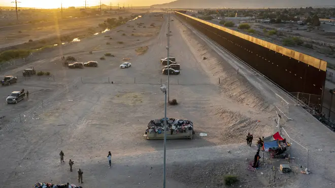 A small group of migrants, bottom right, are pictured while camping outside a gate in the border fence in El Paso, Texas