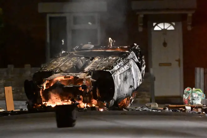 An overturned burnt-out car during rioting on the estate