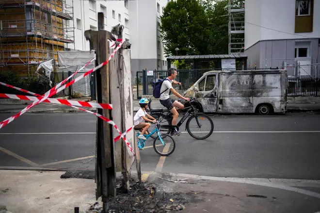 People ride their bicycles past a burned van and destroyed urban items on the aftermath of protests in Colombes, outside Paris, Saturday, July 1, 2023.