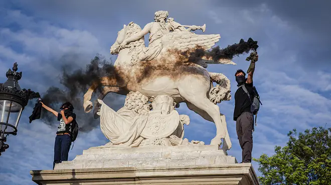 Protesters in France standing on a statue with black gas canisters