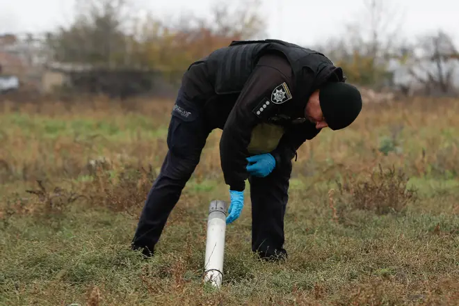 A Ukrainian war crimes investigator inspects a remain of what is believed to be a cluster bomb in Kherson Oblast