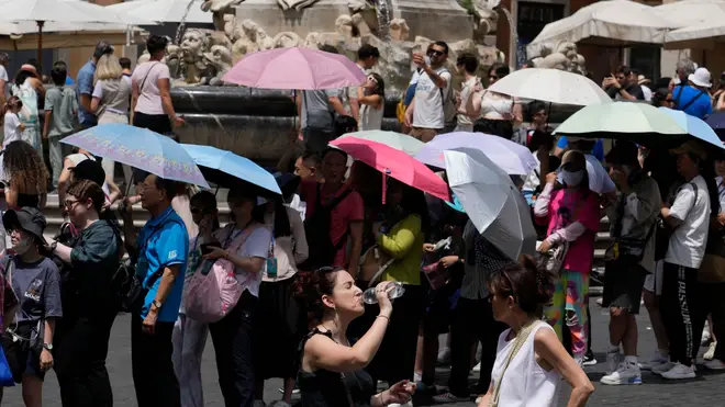 Tourists use umbrellas to shelter from the sun as they queue to enter the Pantheon in Rome