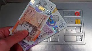 A person holding £30 by a cash machine