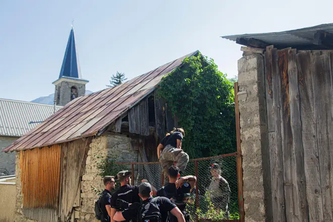 Search teams climb a fence in the village of Vernet in France as they search for Emile
