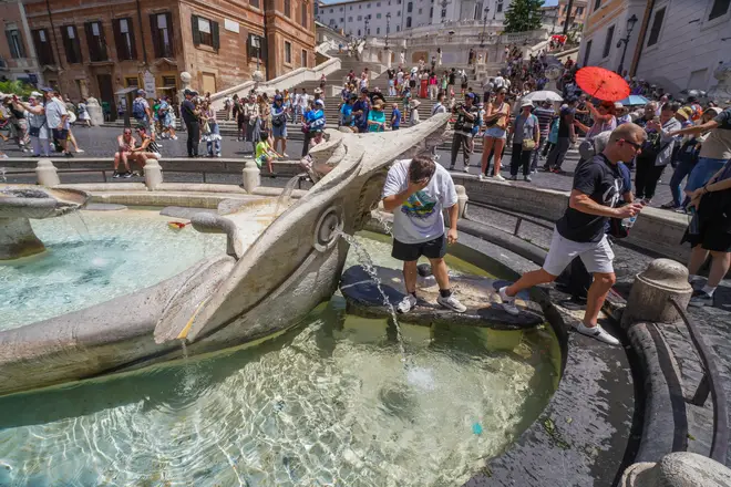 People fill water bottle at the Fontana della Barcaccia on another sweltering day with high temperatures in Rome