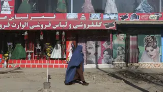 A woman walks past a beauty salon and dress shop in Kabul