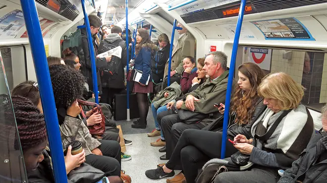 Commuters sitting and standing on a busy tube