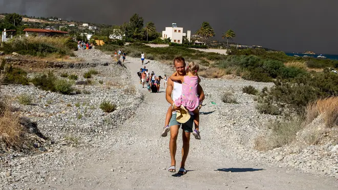 A man carries a child as they leave an area where a forest fire burns