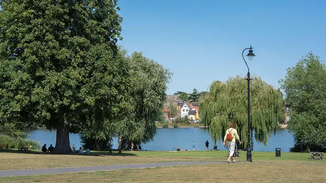 Sunny UK park with lake and people walking