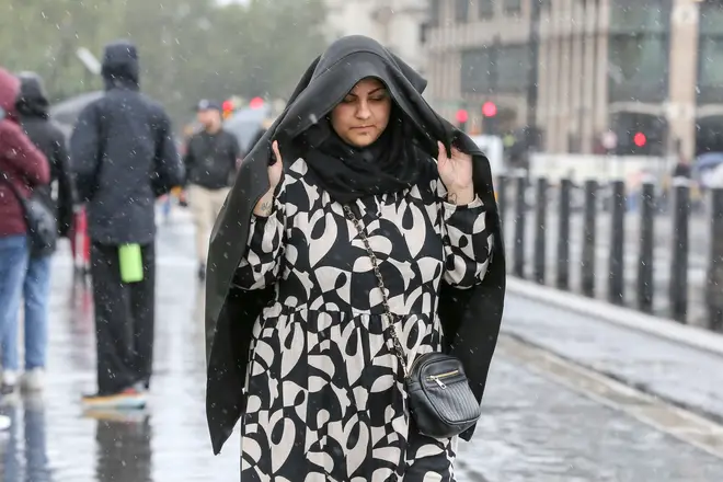 A woman covers her head with a coat as she walks in the rain...