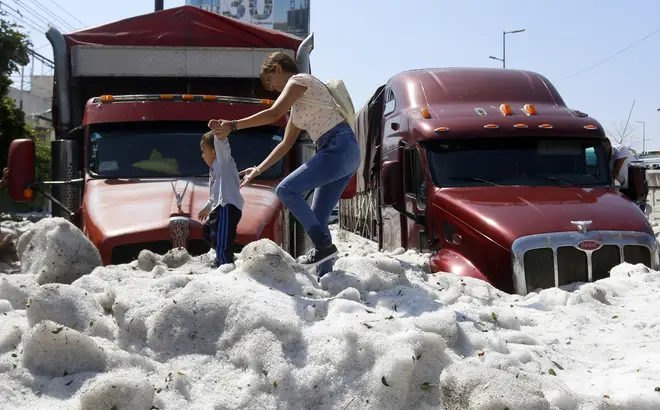 A woman and child walked across a metre-high layer of ice after a freak hailstorm in Mexico