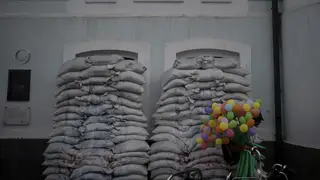 A balloon-seller next to piles of sandbags blocking windows of a building in Kyiv