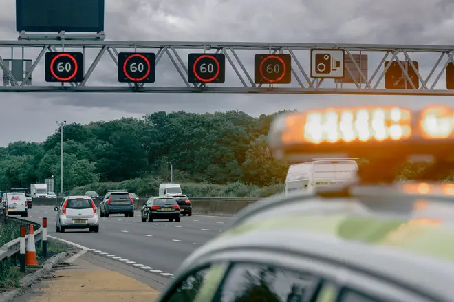 Variable speed signs showing a 60 mph speed limit on a gantry over a smart motorway with National Highways vehicle in foreground in England.