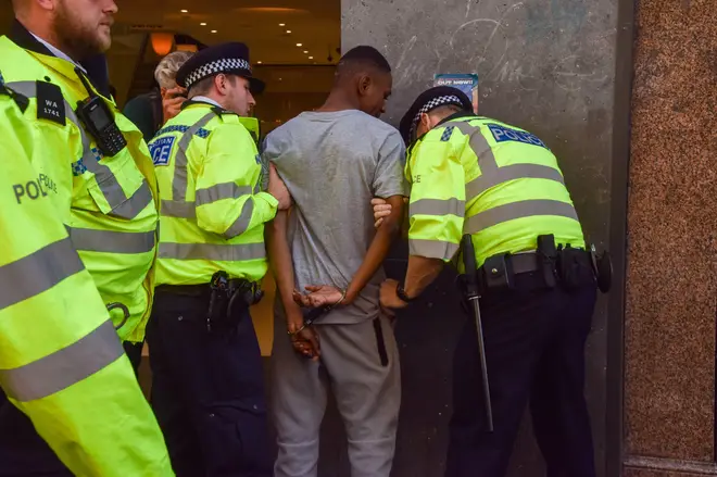 Police officers detain a young man on Oxford Street after a mass shoplifting event.
