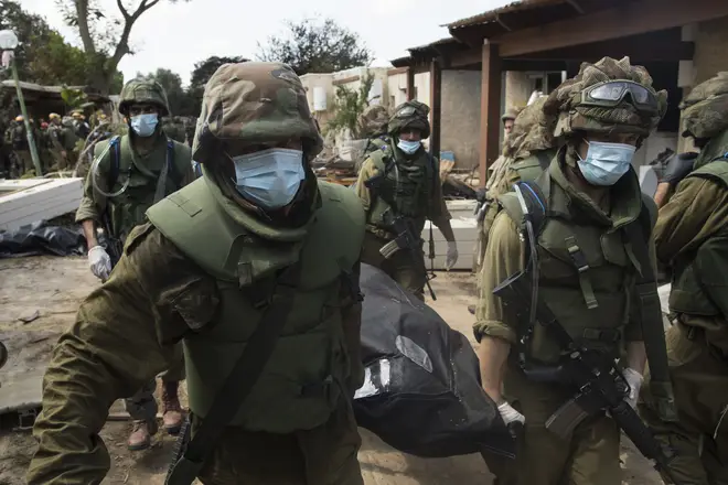 Israeli soldiers carry away the body of a murdered civilian from the Kfar Aza kibbutz