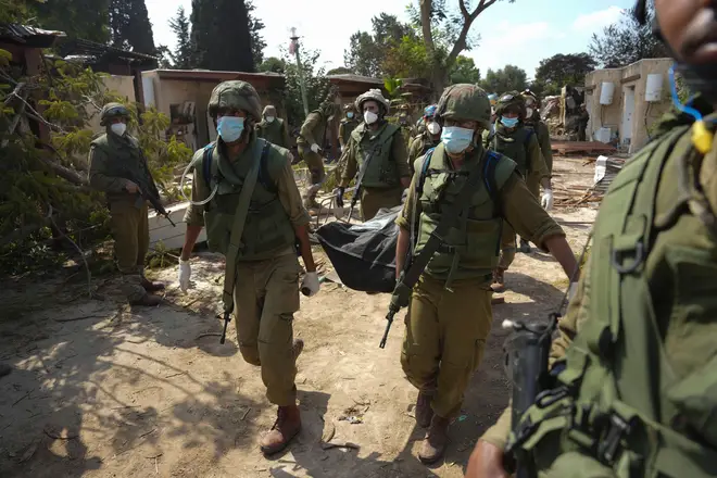 Israeli soldiers carry the body of a person killed in the Hamas attack in kibbutz Kfar Azza on Tuesday, Oct. 10, 2023.