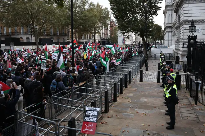 Police officers look on as protesters hold up placards and wave Palestinian flags at the gates of Downing Street