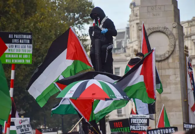 Protesters climb on traffic lights with Palestinian flags next to The Cenotaph in Whitehall. Tens of thousands of people marched in central London in solidarity with Palestine as the Israel-Hamas war intensifies.