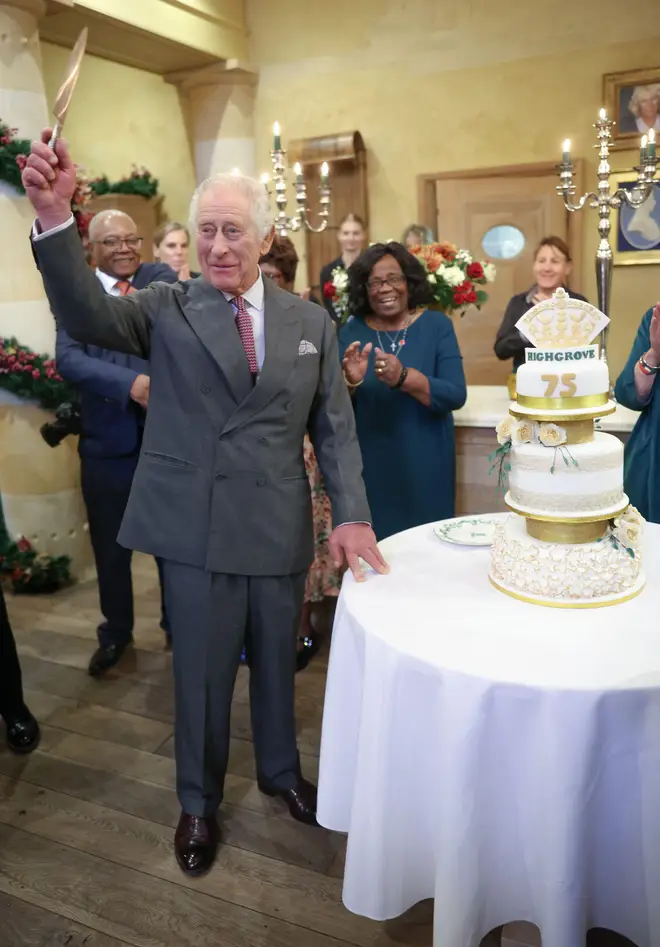 King Charles III holding a knife in the air next to a birthday cake during his 75th birthday party at Highgrove Gardens in Tetbury on the eve of his birthday