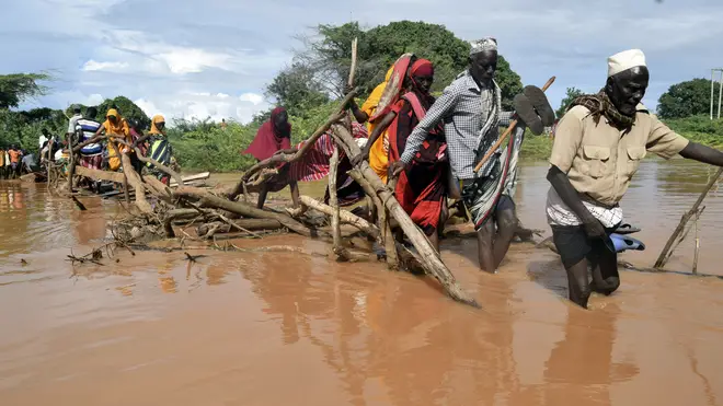 Residents of Chamwana Muma village walk through floodwater after using a makeshift bridge to cross the swollen River Tana, in Tana Delta, Kenya
