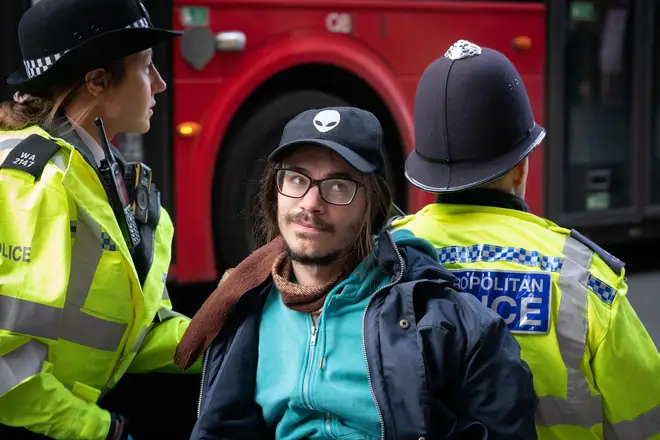 Eco protester in handcuffs sits back to back with a police officer