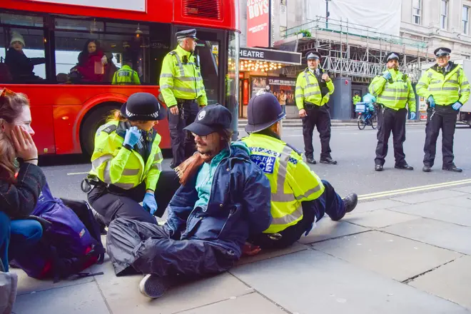 Eco protesters lean against police officers as they sit handcuffed