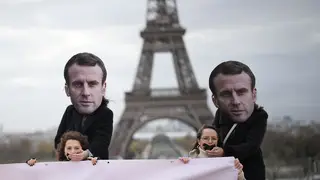 Gagged activists hold a placard as persons wearing a mask of French President Emmanuel Macron stand behind