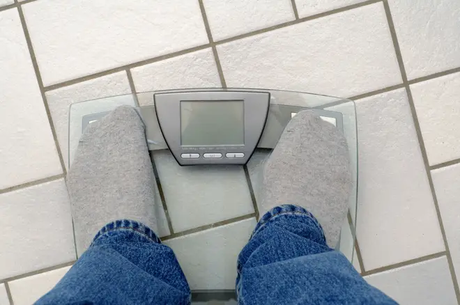 The jeans and socks of a man standing on a scale. Text window on scale free for your own text.