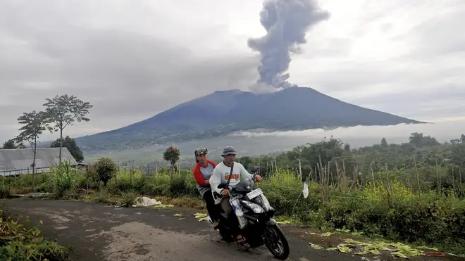 Two people on a motorcycle ride past as Mount Marapi spews volcanic material