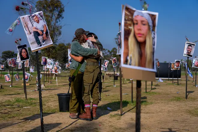 Israeli soldiers embrace next to photos of people killed and taken captive by Hamas militants during their violent rampage through the Nova music festival