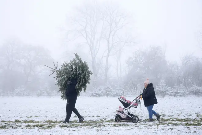 Man carries a Christmas tree across a snow covered field with his partner in Bodsham earlier this month