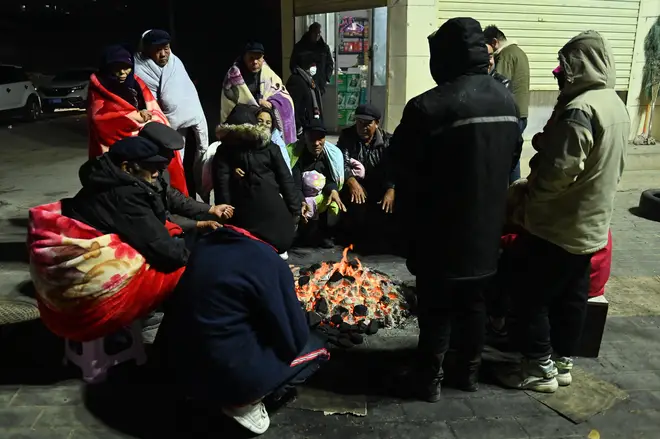 Residents warm themselves around a fire in cold weather conditions