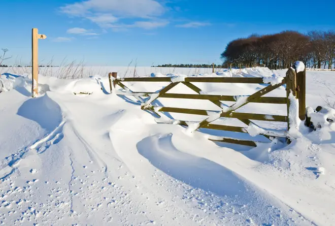 Drifting snow covering a gate, public footpath sign, walls and fields Derbyshire peak district England