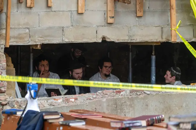 Hasidic Jewish students sit behind a breach in the wall of a synagogue that led to a tunnel dug by the students