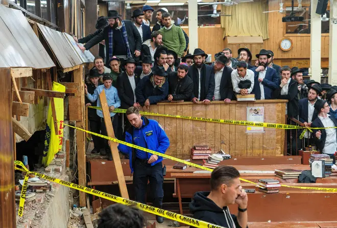 Hasidic Jewish students observe as law enforcement establishes a perimeter around a breached wall in the synagogue that led to a tunnel dug by students