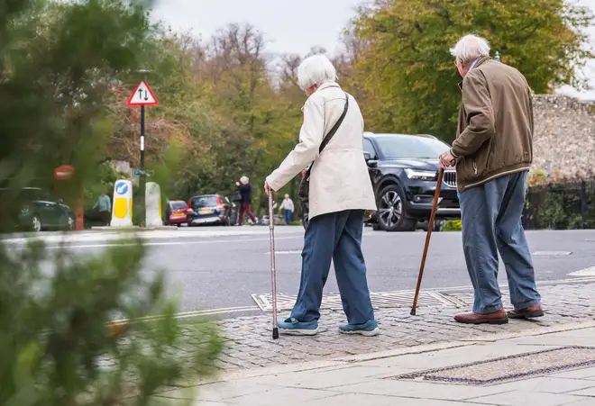 Senior couple of people with walking sticks crossing a road in the UK