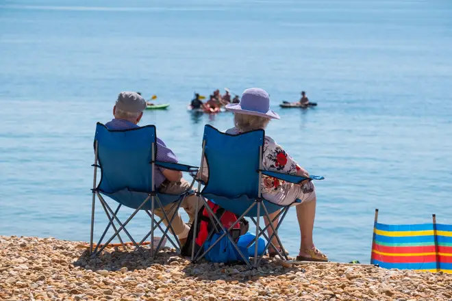 Pensioners sitting on the beach at Lyme Regis, Dorset, UK