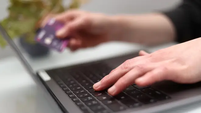 A woman using a laptop and holding a bank card