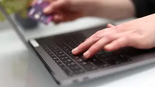 A woman using a laptop and holding a bank card