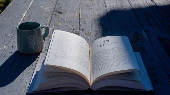 An open book and a mug on an old, rustic-looking porch.