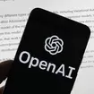 The OpenAI logo on a mobile phone in front of a computer screen displaying output from ChatGPT
