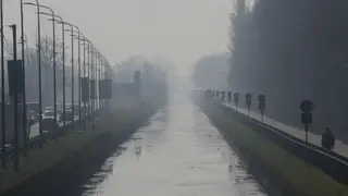 A man walks along the Naviglio Pavese canal shrouded in mist and smog in Milan, Italy