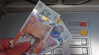A person holding £30 by a cash machine
