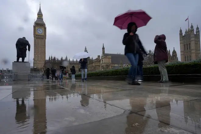 Tourists hold umbrellas against the rain as they walk in Parliament Square next to the Houses of Parliament in London, Thursday