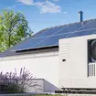 An installed heat pump with photovoltaic panels on the roof of a house, with wind turbine in the background