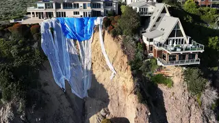 Aerial view of mansions still standing along a cliff after a portion of the cliffside (L) tumbled to the Pacific Ocean following days of heavy rains earlier this month on February 27, 2024 in Dana Point, California
