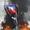A man holds up a Haitian flag as tyres burn behind him