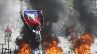 A man holds up a Haitian flag as tyres burn behind him